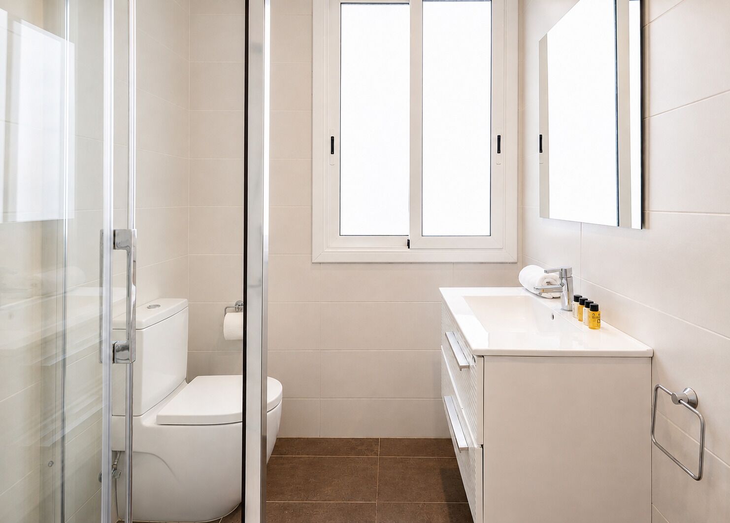 A bathroom with a toilet, a shower enclosure, a sink with toiletries, and a window.