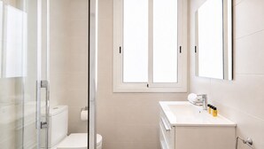 Un baño con inodoro, cabina de ducha, lavamanos y amenities, y una ventana.