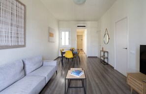 Een moderne woonkamer met een grijze bank, een klein bijzettafeltje en een eethoek met gele stoelen.