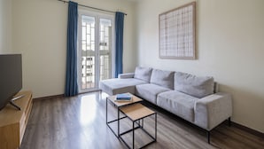 Una sala de estar moderna con un sofá gris, una pequeña mesa de centro negra y un televisor sobre un soporte de madera.