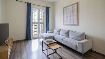 Un salon moderne avec un canapé gris, une petite table basse noire et un téléviseur posé sur un meuble en bois.