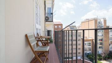 Un balcon avec une table et des chaises, une vue sur les bâtiments voisins et un ciel dégagé.