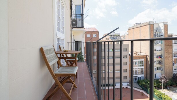 Un balcón con mesa y sillas, vista a edificios vecinos y cielo despejado.