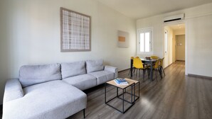 A modern living room with a grey sectional sofa, a small coffee table, and a dining area with yellow chairs. - Stay U-nique Apartments Sagrada Familia (Barcelona)
