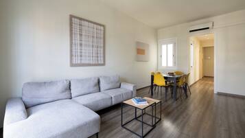Un salon moderne avec un canapé d’angle gris, une petite table basse et un coin repas avec des chaises jaunes.