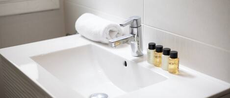 A white bathroom sink with a modern faucet, a rolled white towel, and four bottles of toiletries.