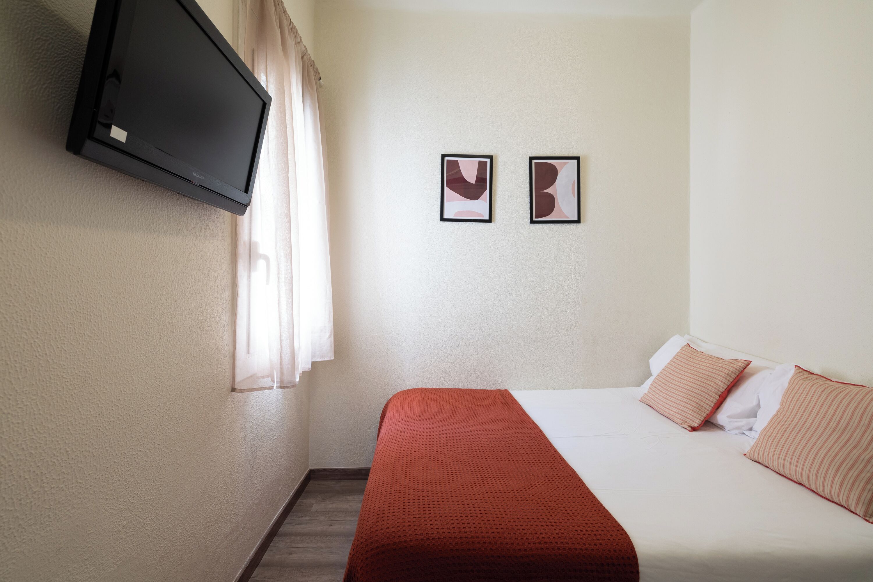 A hotel room with a bed, a TV mounted on the wall, and two framed pictures on the wall.