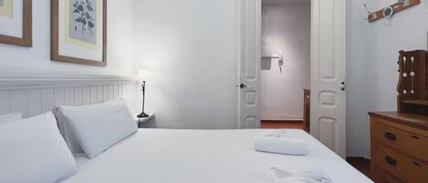 Een hotelkamer met een net opgemaakt bed, een bedlamp, een houten dressoir en een deur naar een badkamer.