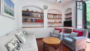Een woonkamer met een bank, fauteuils, een houten salontafel en boekenplanken.