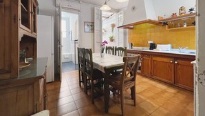 Een keuken met houten kastjes, een eettafel met stoelen en een betegelde vloer.