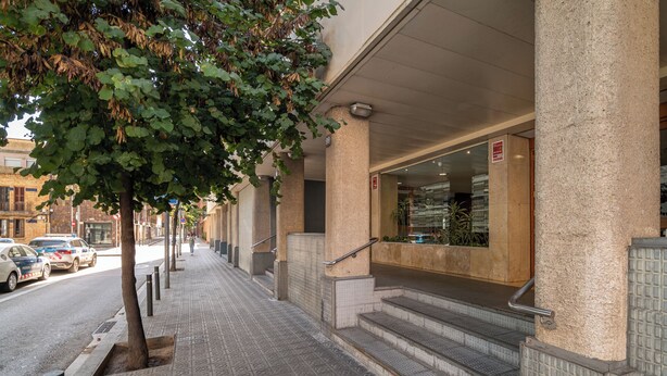 Une entrée d’immeuble avec un chemin recouvert de carreaux, un arbre et un escalier menant à l’entrée.