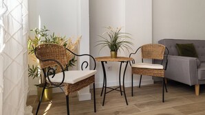 Une pièce d’angle avec un canapé gris, deux fauteuils en osier, une petite table et des plantes en pot.