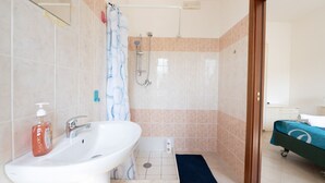 Une salle de bain avec un lavabo, une douche et un lit recouvert d’une couverture bleue.
