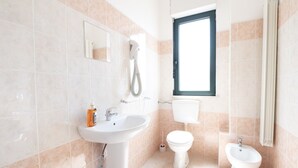 Une salle de bain équipée d’un lavabo, de toilettes, d’un bidet et d’une fenêtre.