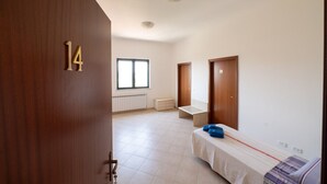 Une pièce avec un lit, une fenêtre, un radiateur et deux portes.
