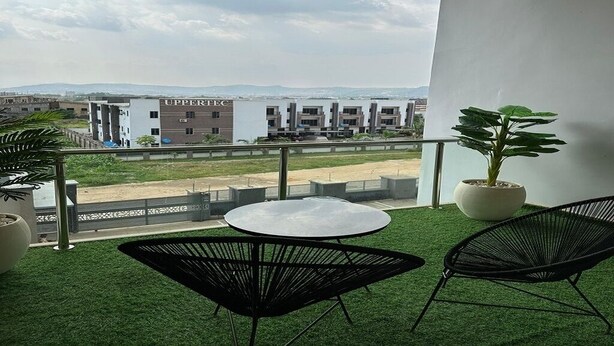 A balcony with artificial grass, two black chairs, a small round table, and potted plants.