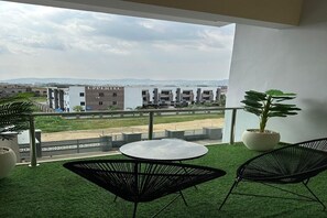 A balcony with artificial grass, two black chairs, a small round table, and potted plants.
