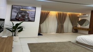 A modern bedroom with a bed, a wall-mounted TV, a potted plant, and a large artwork depicting a figure with the text "I AM BEAUTIFUL."