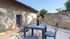 Ein Steinhaus mit einer kleinen Terrasse, ausgestattet mit Tisch und Stühlen, einer Weinflasche und einem Blumentopf.