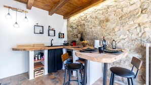 Eine rustikale Küche mit Steinwand, Holzbalken und einer Bar mit Hockern.