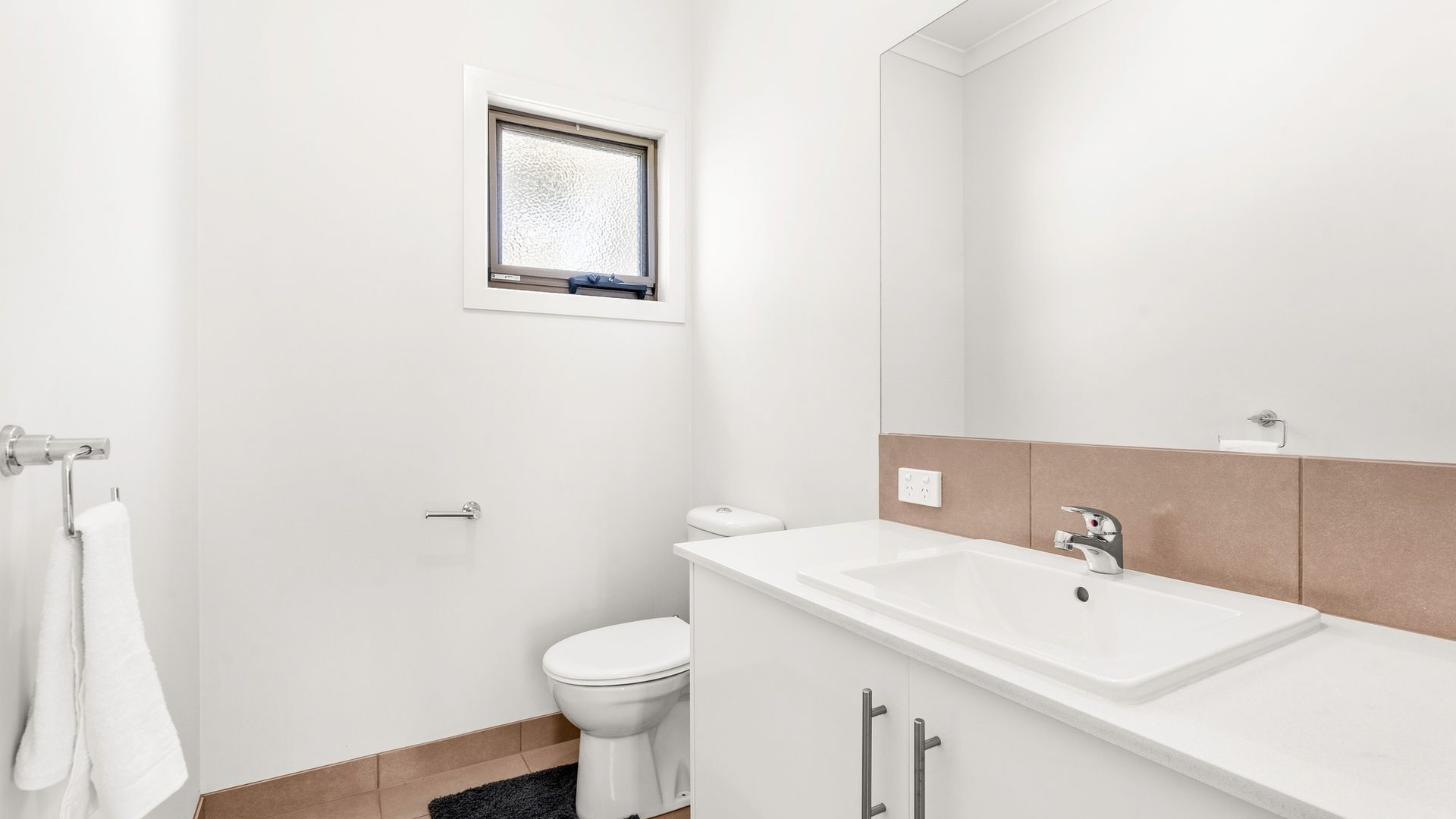 A modern bathroom with a white sink, a toilet, and a window above the toilet.
