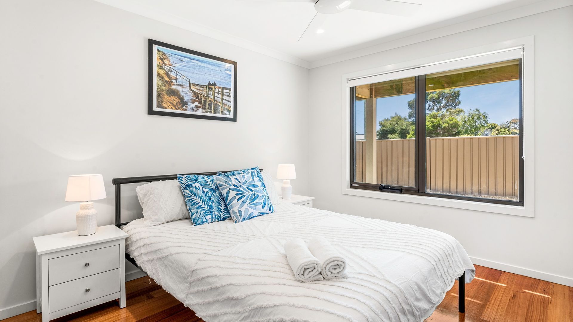 A bedroom with a bed, two bedside tables, a nightstand, a window with a view, and a ceiling fan.