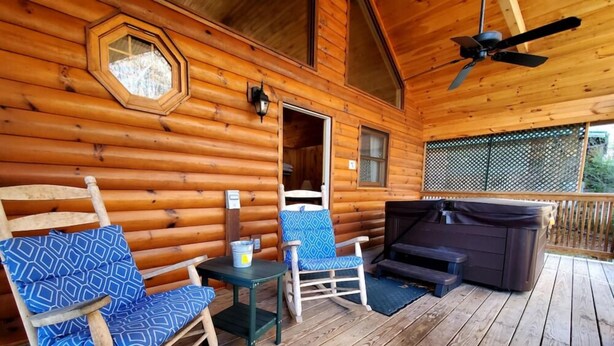 Eine Holzhütte mit Veranda, ausgestattet mit Schaukelstühlen, einem Tisch und einem Whirlpool.