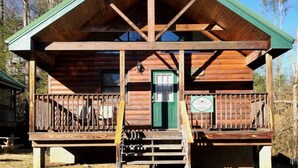 Eine Holzhütte mit grüner Tür, einer Veranda mit Geländern und einem Schild.