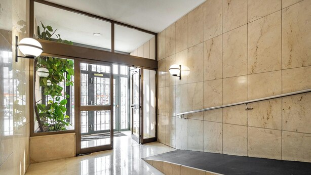 Un hall d’entrée moderne avec une porte d’entrée en verre, une rambarde en métal et une plante en pot.
