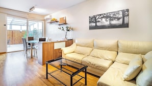 Un salon moderne avec un canapé beige, une table basse en verre et un coin repas comprenant une table et des chaises en bois.