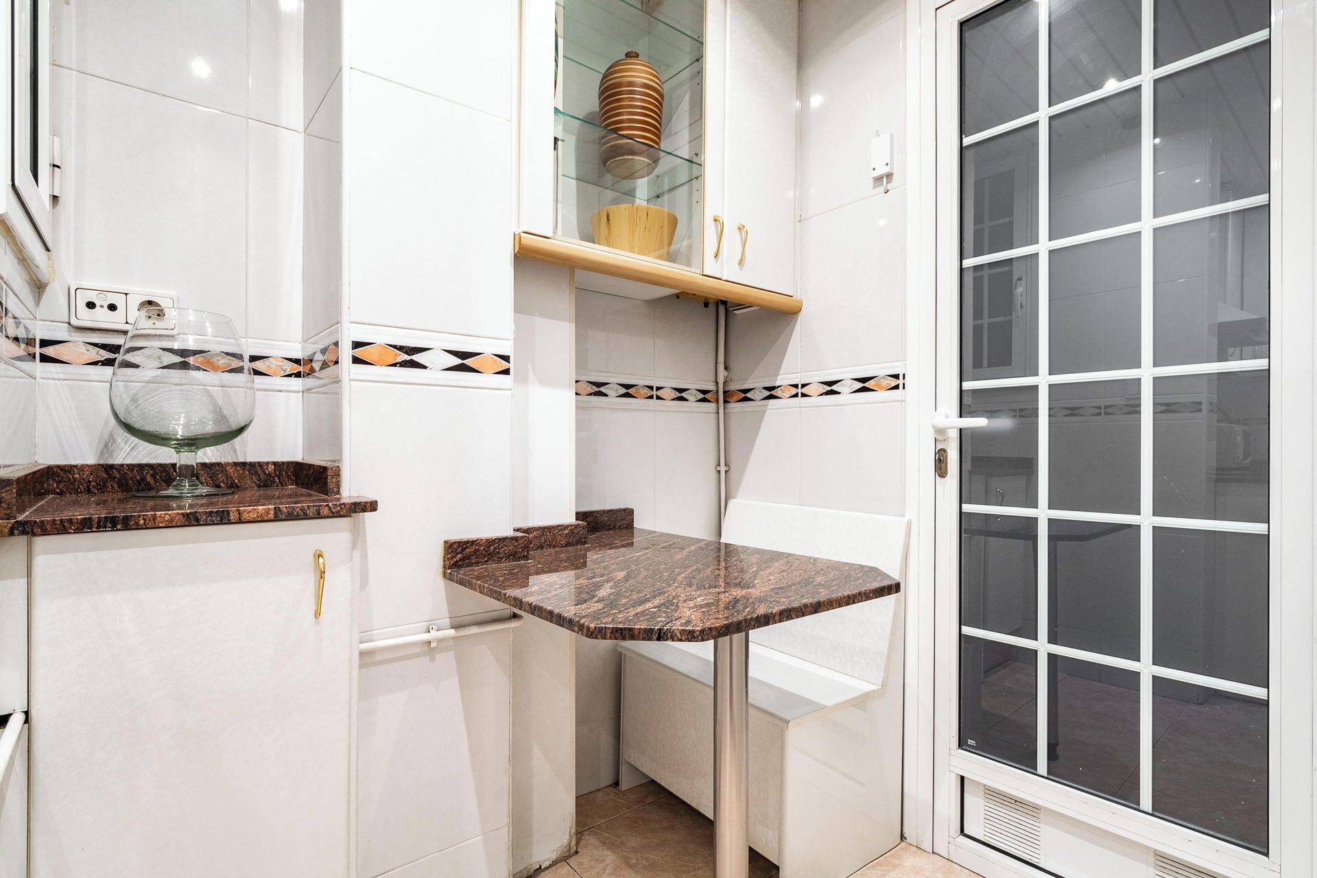 A kitchen with white cabinets, a marble countertop, a glass bowl, and a window with a grid pattern.