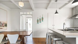 A modern kitchen with a wooden dining table, white chairs, and a bar area with stools.