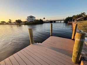 A wooden dock extending into calm water with a bridge in the background.