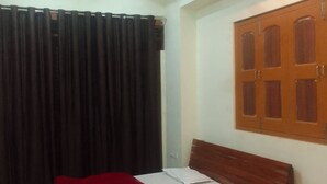 Una habitación con una cama de madera, una manta roja, un ventilador de techo y una ventana con contraventanas de madera.