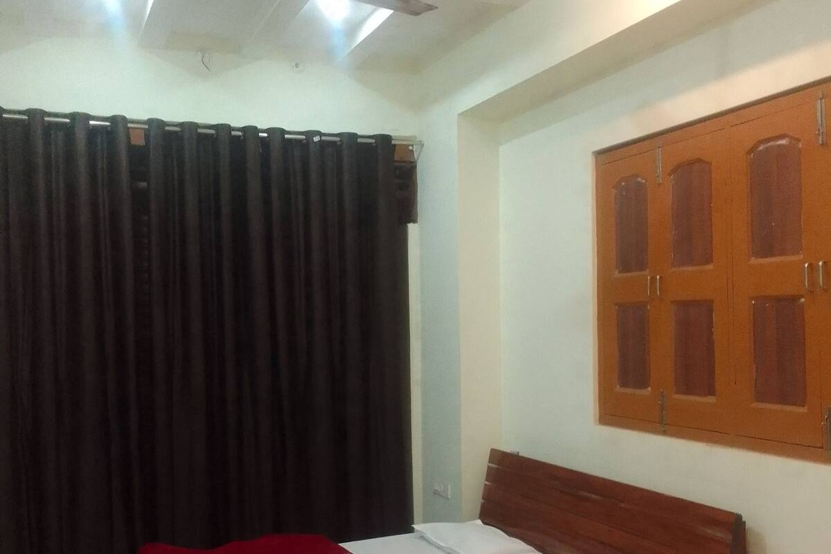 Una habitación con una cama de madera, una manta roja, un ventilador de techo y una ventana con contraventanas de madera.