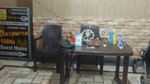 Una habitación con suelo de baldosas, una mesa de madera con un cuadro enmarcado, una silla y una pequeña estatua. Hay un cartel en la pared que anuncia una casa de huéspedes.