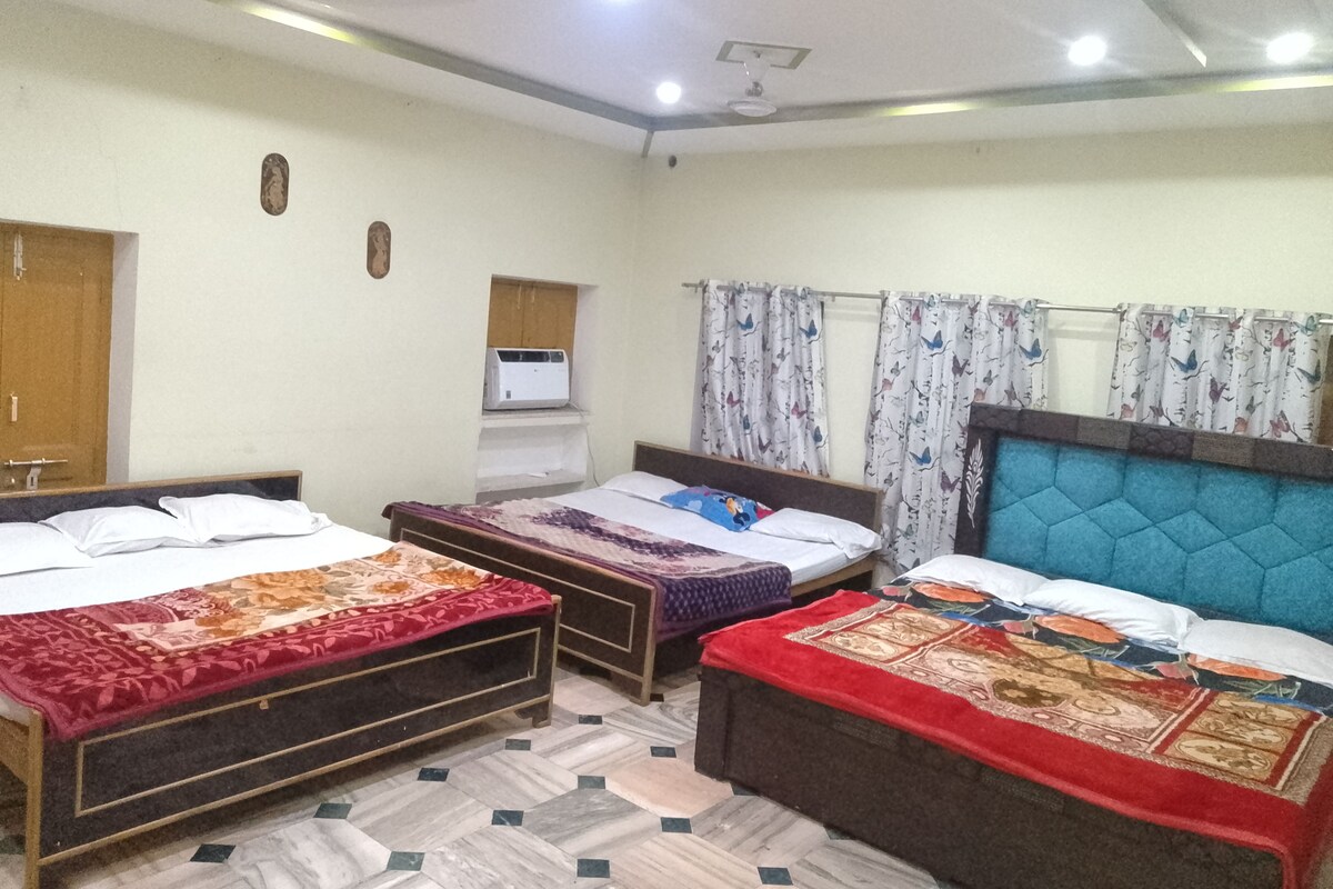 A room with three beds, a ceiling fan, a wall-mounted air conditioner, and patterned curtains.