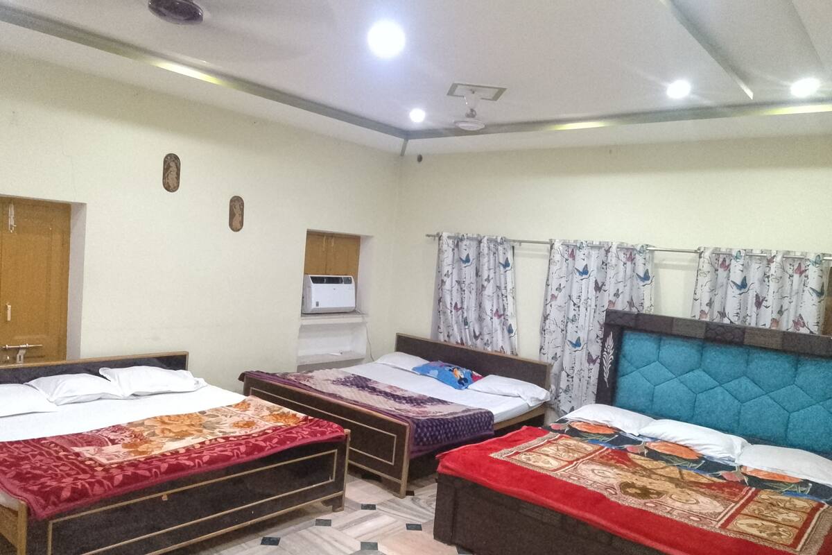 Una habitación con tres camas, ventilador de techo, aire acondicionado instalado en la pared y cortinas estampadas.