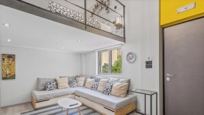 A modern living room with a sectional sofa, a small round table, and a glass coffee table. There is a balcony with a railing and a door to the right.