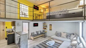 A modern loft apartment with a kitchen, a dining area, a living room with a sofa and a TV, and a balcony with a bed.