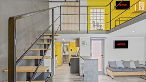 A modern interior with a staircase, a kitchen area, a seating area with a sofa, and a TV labeled "NETFLIX".