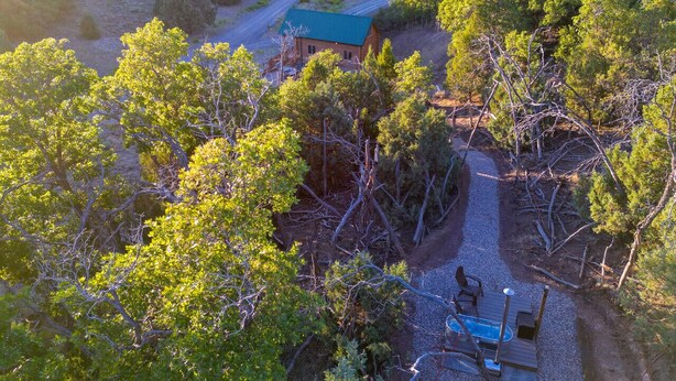 An aerial view of a cabin surrounded by dense forest, with a gravel path leading to a wooden deck and a pool. - Bryce and Zion middle point with Cowboy Hot tub (Alton)