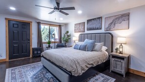 A bedroom with a bed, a ceiling fan, a nightstand, a lamp, and artwork on the wall. - National Parks - Cowboy Hot tub and UFO Sightings (Alton)