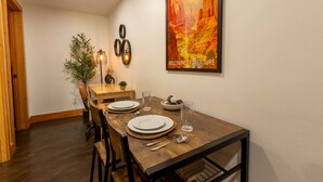 A dining area with a wooden table set for two, a poster on the wall, and a plant in the corner. - National Parks - Cowboy Hot tub and UFO Sightings (Alton)