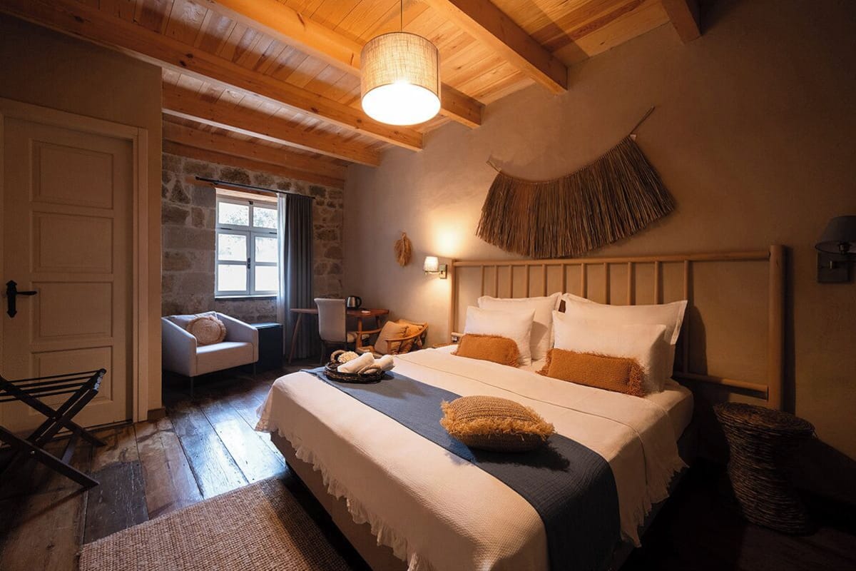 A cozy bedroom with a large bed, a stone wall, a hanging basket, and a wooden ceiling.