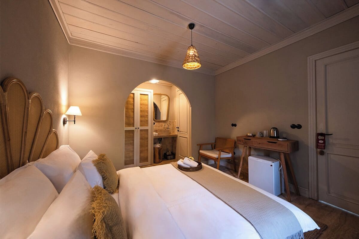 A hotel room with two beds, a desk, a chair, a small refrigerator, and a bathroom with a mirror and sink.