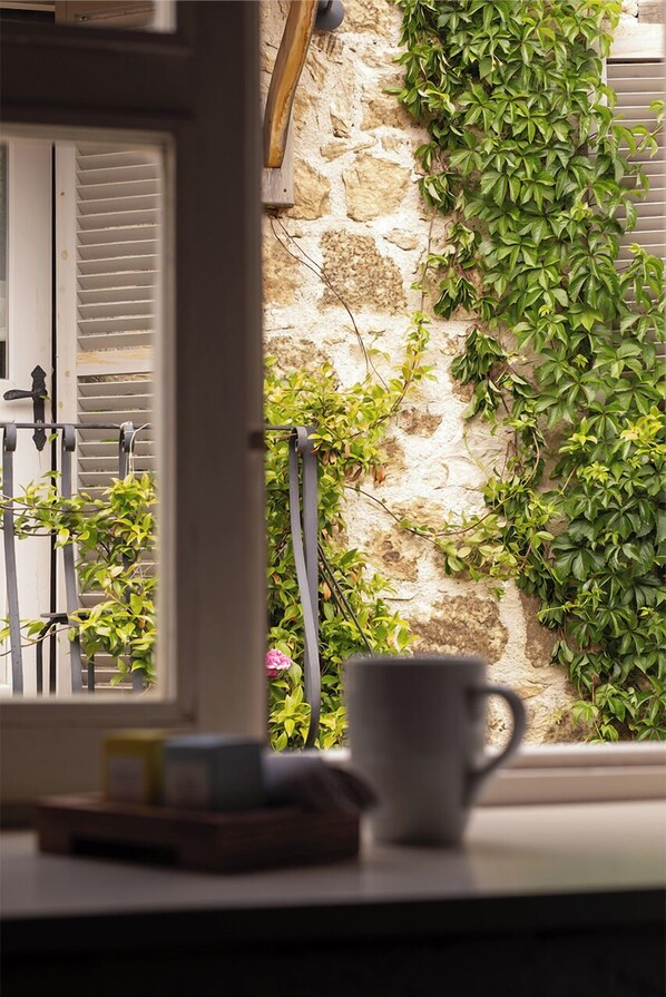 A window with a white cup on the sill, a metal railing, and a stone wall with green ivy.