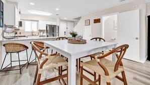 A modern kitchen with white cabinets, stainless steel appliances, and a large island with chairs. - Gulf Highlands 229- St. Katherine Blvd (Panama City Beach)
