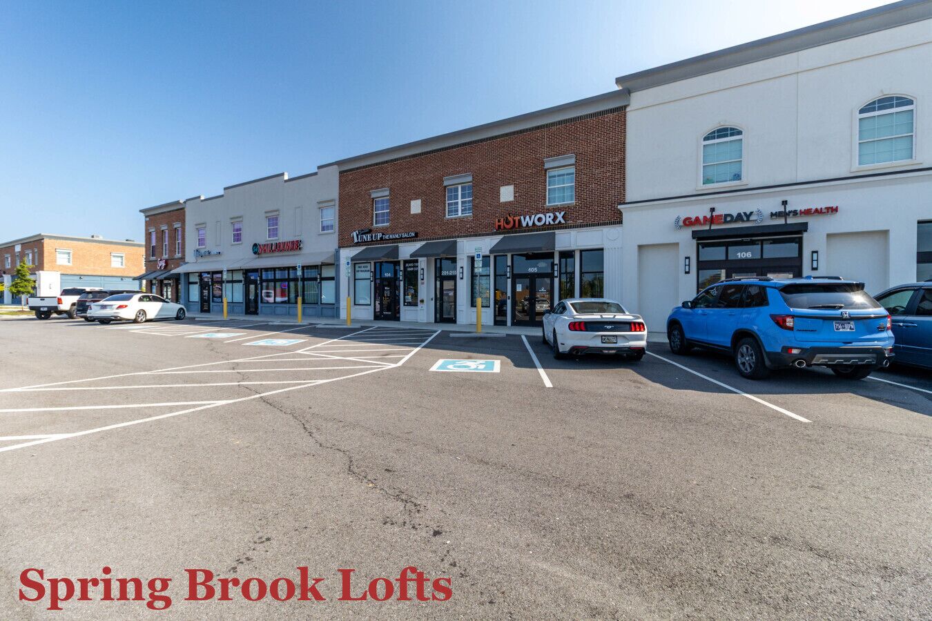 A parking lot with several cars and a building with storefronts including 'Lune Up The Daily Salon' and 'Men's Health'.
