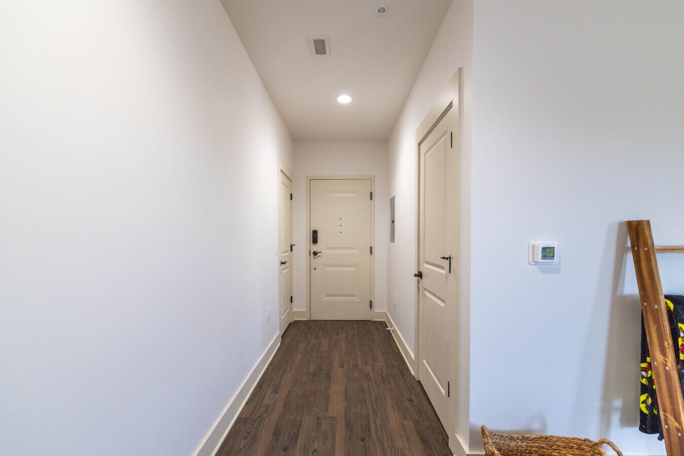 A narrow hallway with wooden flooring, white walls, and a closed door at the end.